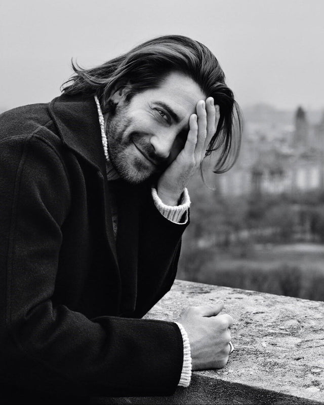 Jake Gyllenhaal leaning on a railing with a blurred scenic background wearing a Stephen Einhorn signet ring
